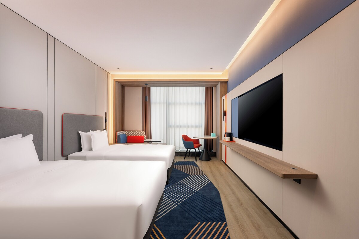 A hotel room with two beds, a TV, a desk, and a chair.