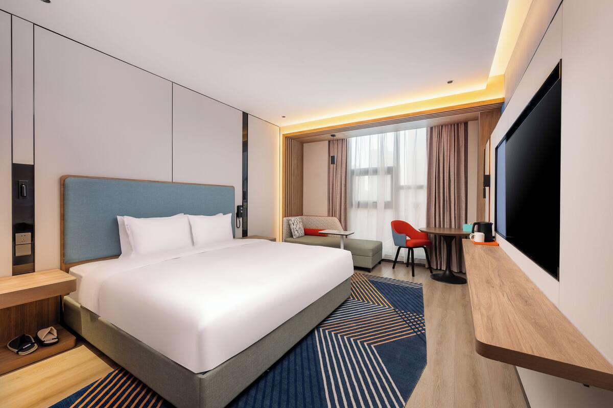 A hotel room with a large bed, a desk, a TV, and a seating area with a chair and table.
