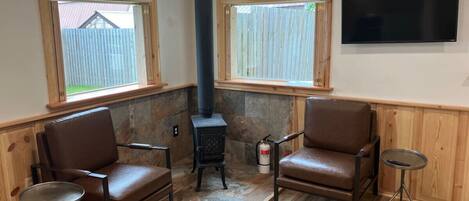 A cozy room with two leather chairs, a small table, a TV, and a wood-burning stove.