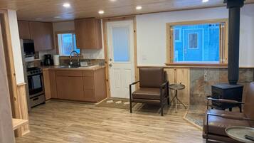 A compact kitchen with wooden cabinets, a built-in oven, and a stove. There is a dining area with a table and chairs, and a large window providing natural light.