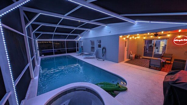 Una piscina interior con jacuzzi, rodeada por una zona techada con asientos y un letrero de neón.