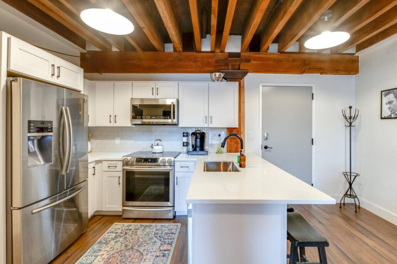 A modern kitchen with stainless steel appliances, white cabinetry, and a wooden ceiling.