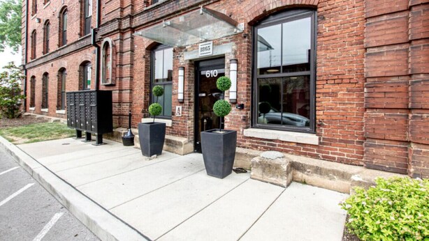 A brick building with a large glass entrance, numbered 610, and two potted plants outside. - Stylish Apartment with Urban Charm (Nashville)
