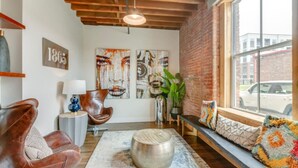 A cozy living room with a leather sofa, a round coffee table, and a large window with a view of the street. - Stylish Apartment with Urban Charm (Nashville)