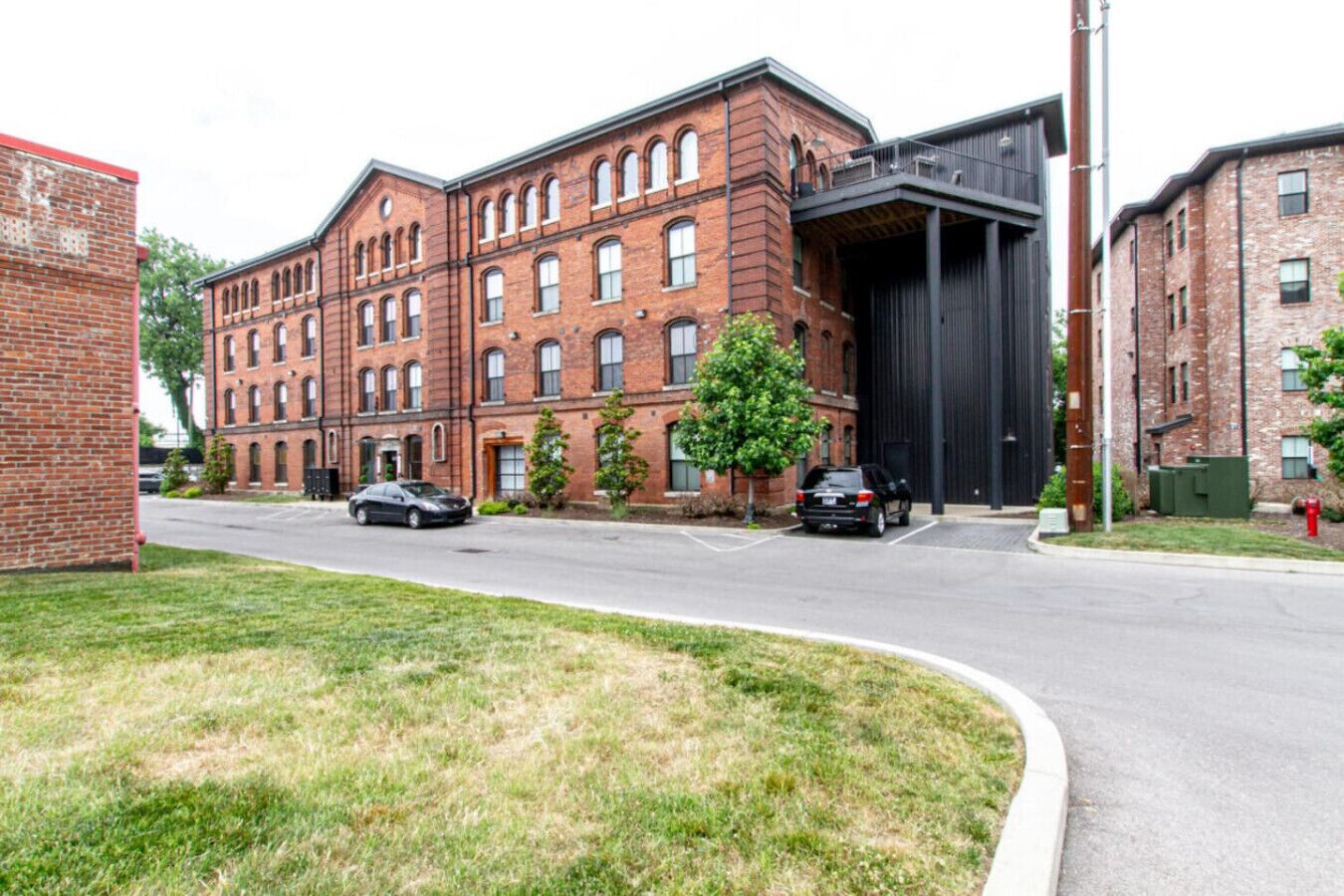 A multi-story brick building with a large garage door, parked cars, and a grassy area in the foreground.