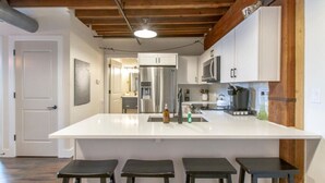 A modern kitchen with a large island, stainless steel appliances, and wooden beams on the ceiling. - Stylish Apartment with Urban Charm (Nashville)