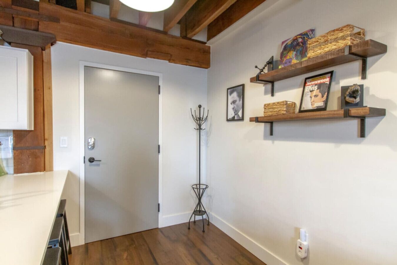 A hallway with wooden beams, a white door, and a shelf with magazines and a picture frame.