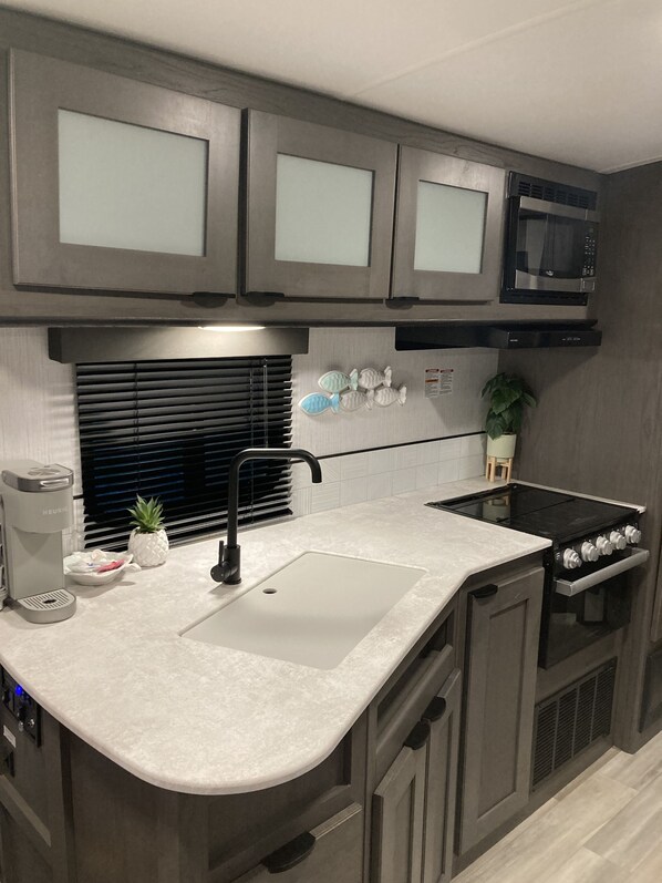 Une cuisine moderne avec des meubles gris, un évier en acier inoxydable, une cuisinière noire et un four à micro-ondes placé au-dessus de la cuisinière.