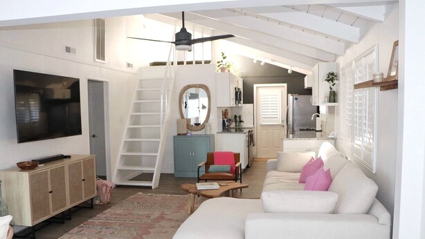 Een ruime woonkamer met een witte bank, een houten kast, een televisie en een trap naar een hoger niveau.