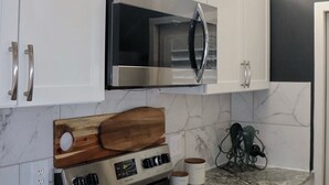 Een keuken met witte kastjes, een roestvrijstalen magnetron, een zwart fornuis en granieten aanrechtbladen.