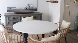 Een eetgedeelte met een ronde tafel, rieten stoelen, een plafondventilator en een tv aan de muur.