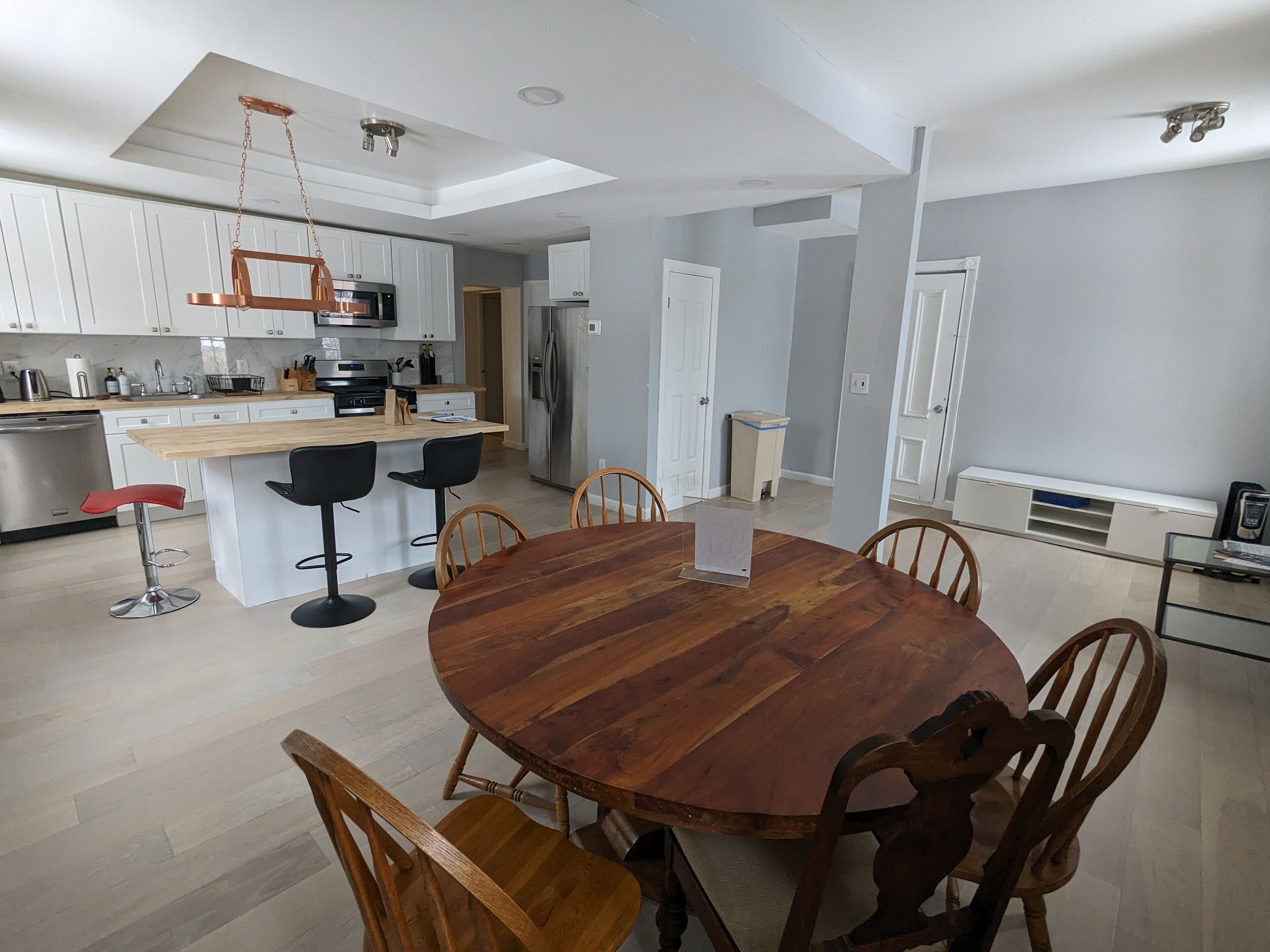 A modern kitchen with white cabinets, a wooden dining table, and bar stools.