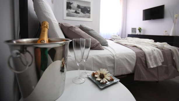 Une chambre d’hôtel avec un lit, une table de chevet sur laquelle se trouve une bouteille de champagne, deux verres et une assiette décorative.