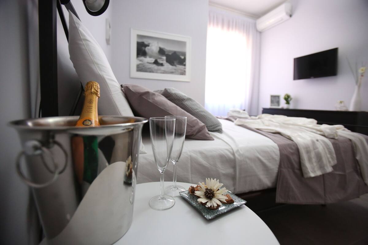 Ein Hotelzimmer mit einem Bett, einem Nachttisch mit Champagnerflasche, zwei Gläsern und einer dekorativen Platte.