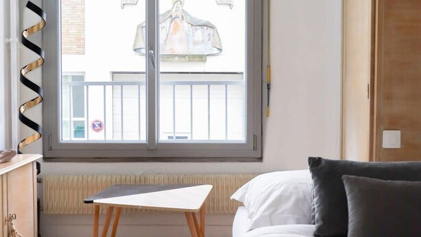 Une chambre à coucher comprenant un lit, une petite table, un radiateur et une fenêtre donnant sur un balcon.