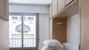 Une petite chambre à coucher moderne, avec un lit, une petite table et une fenêtre donnant sur un bâtiment à l’extérieur.