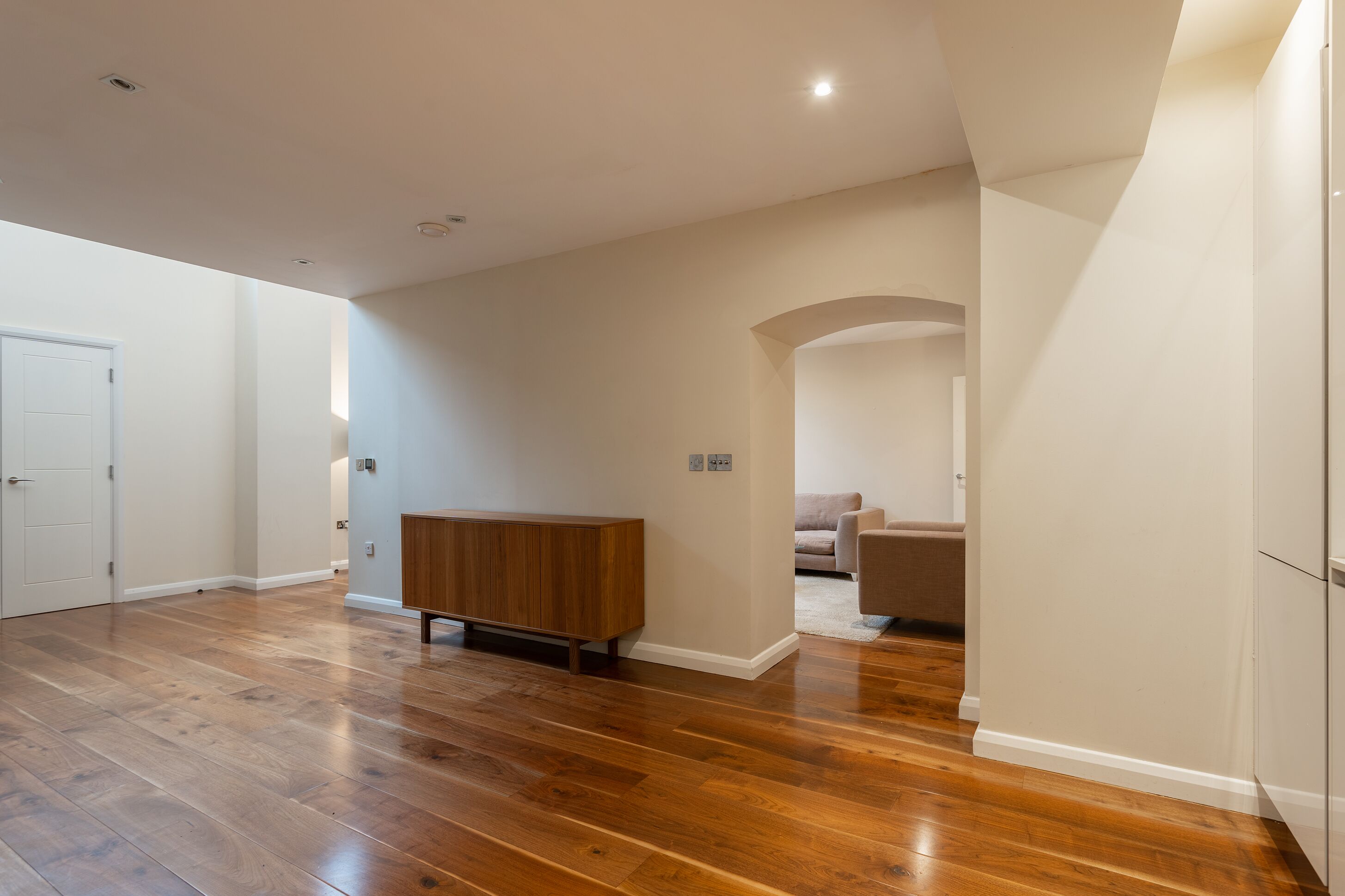 A spacious room with hardwood flooring, a wooden bench, and a doorway leading to another room.