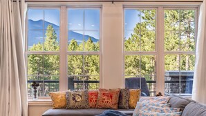 Una habitación con un ventanal que da a un paisaje montañoso, un sofá con cojines estampados y vistas a un patio.