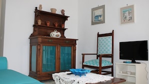 A living room with a sofa, a wooden cabinet with pottery, a blue chair, a television, and a table with a blue bowl.