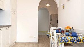 A narrow kitchen with white cabinets and a dining area with a table set for two.