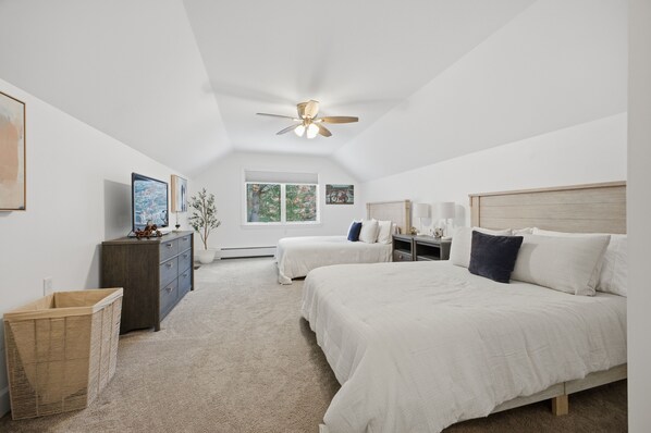 A bedroom with two beds, a ceiling fan, a dresser, a window, and a wall-mounted TV.