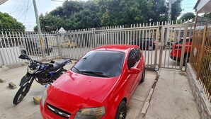 A red car parked in a gated area with a motorcycle beside it. - Apartamento Acogedor en Edificio Privado, el Placer de Sentirse Como en Casa!!! (Barranquilla)