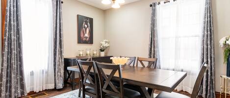 A dining area with a wooden table and chairs, a chandelier, and curtains.