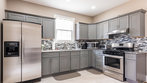 A modern kitchen with stainless steel appliances, grey cabinets, and a tiled backsplash. - Valhalla View Home-Minutes to Golf Course-Perfect for Golfers, Horses, Trailers (Louisville)