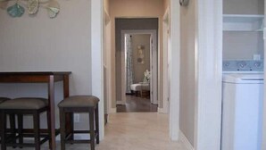 A hallway with a dining area featuring a wooden table and two chairs, leading to a bedroom with a bed and a nightstand. - Valhalla View Home-Minutes to Golf Course-Perfect for Golfers, Horses, Trailers (Louisville)