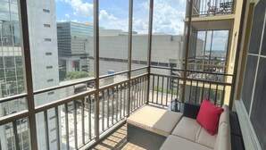 A balcony with a sofa and cushions, large windows, and a view of buildings. - FIFA 2026 Walk to Stadium | 1BR Unit 15L ATL (Atlanta)