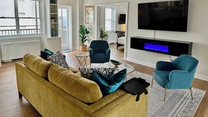 Ein Wohnzimmer mit einer Couch, zwei Sesseln, einem Couchtisch, einem Flachbildfernseher und einem Kamin.