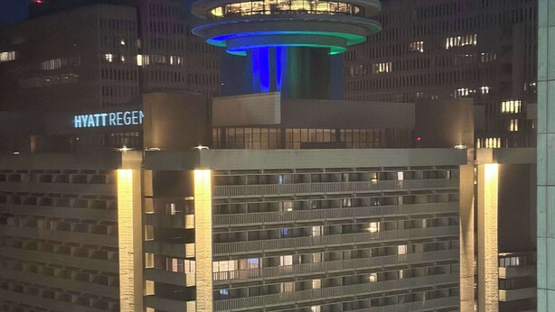 Ein Hochhaus mit einer markanten Kuppelkonstruktion an der Spitze, beleuchtet in Blau.