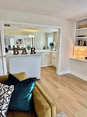 Un intérieur moderne comprenant un espace cuisine, un comptoir de bar avec des lettres illuminées et un coin salon confortable avec un canapé et des coussins.