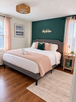 A bedroom with a bed, a bedside table, a wall-mounted light fixture, a framed picture, and a neon sign.