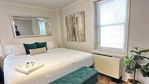 A neatly arranged bedroom with a large bed, a bench, a potted plant, and a radiator. - FIFA 2026 Walk to Stadium | 1BR Unit 7-O ATL (Atlanta)
