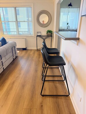 Een moderne keuken met een houten vloer, een zwarte barstoel, een witte bank en een ronde spiegel aan de muur.