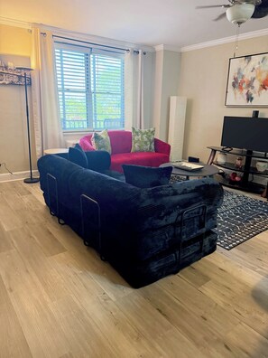 A living room with a large sectional sofa, a flat-screen TV, and a ceiling fan.