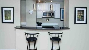 Una cocina moderna con armarios blancos, encimera negra y dos taburetes negros.