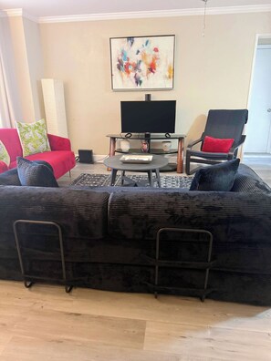 A living room with a black sofa, a red couch, a black chair, a coffee table, and a flat-screen TV on a stand. - FIFA 2026 Walk to Stadium | 1BR Unit 3H ATL (Atlanta)