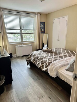 A bedroom with a bed, a radiator, a window with blinds, a door, and a wall-mounted mirror. - FIFA 2026 Walk to Stadium | 1BR Unit 3H ATL (Atlanta)
