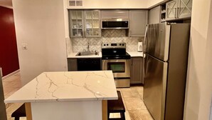 Una cocina con encimera de mármol, electrodomésticos de acero inoxidable y salpicadero con diseño de espiga.