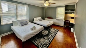 Habitación con dos camas, ventilador de techo, escritorio, silla y ventana con persianas.