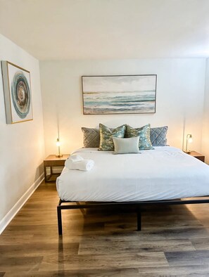 Quarto com cama, almofadas, um quadro e luminárias de cabeceira.