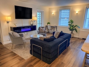 A modern living room with a flat-screen TV, a sofa, a coffee table, and a dining area.