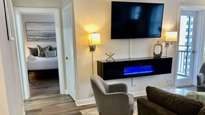 A modern living room with a flat-screen TV, a sofa, a chair, and a bed with a painting.