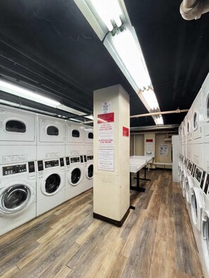 A laundry facility with multiple washing machines, a central pillar with posted guidelines, and a wooden floor. - FIFA 2026 Walk to Stadium | 1BR Unit 12K ATL (Atlanta)