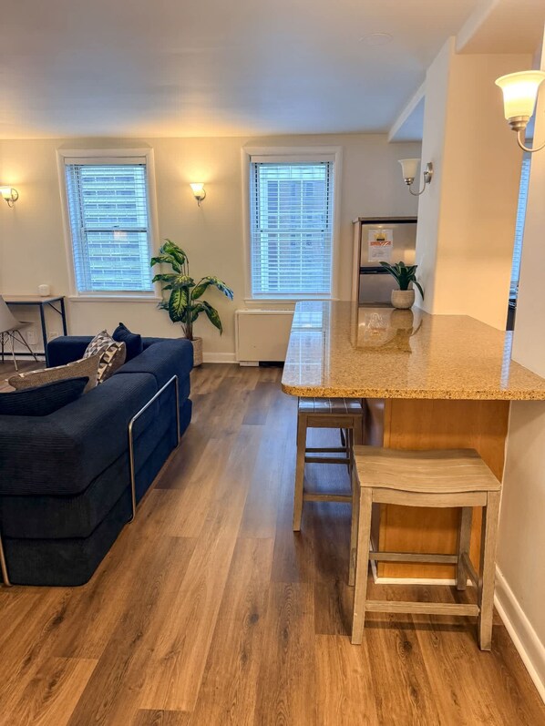A modern kitchen with a wooden countertop, a bar stool, and a dining area with a blue sofa.