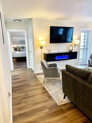 A modern living room with a flat-screen TV, a grey armchair, a brown sofa, and a wooden floor. - FIFA 2026 Walk to Stadium | 1BR Unit 12K ATL (Atlanta)