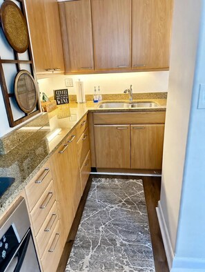 Une cuisine avec des meubles en bois, un plan de travail en granit, un évier en acier inoxydable et un tapis à motifs de marbre.
