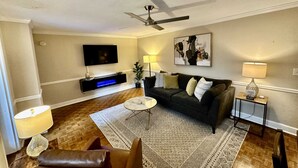 A living room with a ceiling fan, a flat-screen TV, a dark-colored sofa, a patterned rug, and a small side table with a lamp. - FIFA 2026 Walk to Stadium | 2BR Unit 4G ATL (Atlanta)